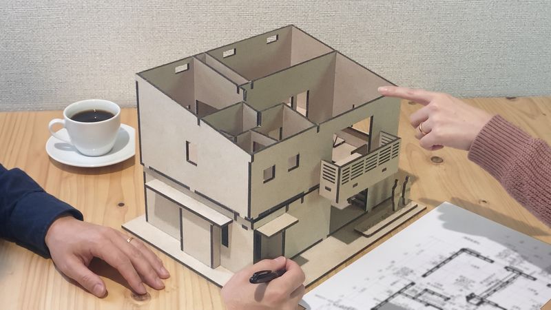 打ち合わせのテーブルで、模型のバルコニーを指さしている手元